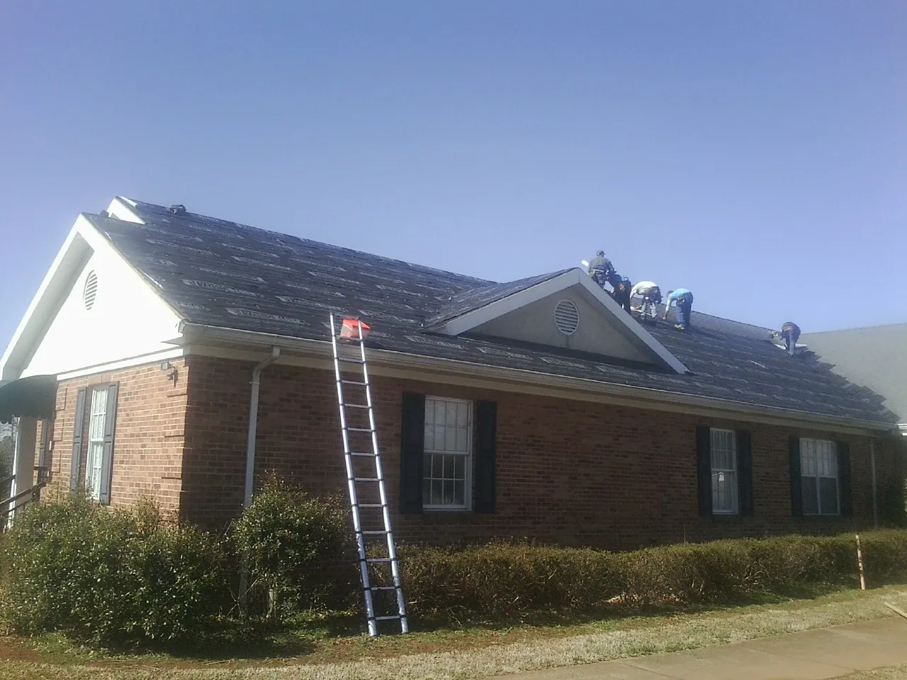 Crew tearing shingles off a brick ranch roof with a ladder set — Metal Roof Repair work by our crew in Hiram