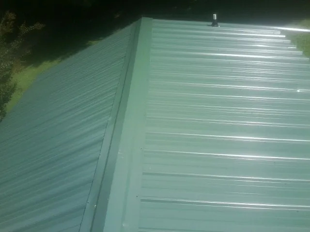 New green metal panels meeting at the ridge of a roof — Flat Roof Repair work by our crew in Hiram