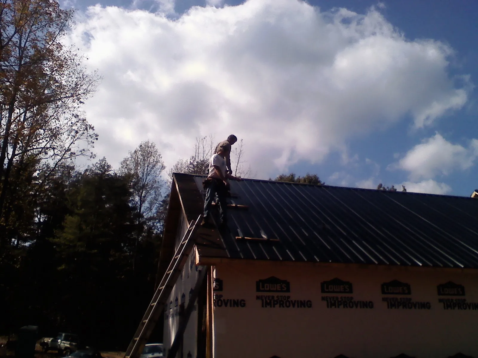 Roofer fastening dark metal panels high against a cloudy sky, from a Roof Inspection job in Hiram